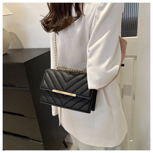 Model wearing a black quilted leather crossbody bag with gold chain and V-pattern stitching