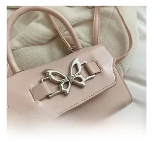 Detailed close-up of pink glossy handbag with a silver butterfly-shaped metal clasp