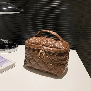 Brown quilted puffer handbag with padded handle and dual metal zippers on white table