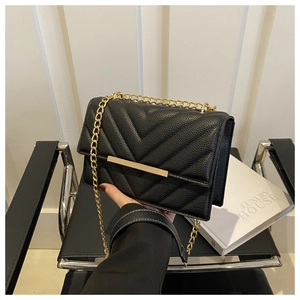 Macro detail of the elegant black quilted V-pattern leather and gold metal chain strap