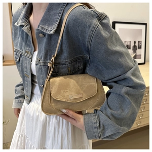 Detail of khaki suede shoulder bag with silver plaque and adjustable strap on a model
