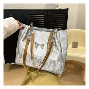 Detailed view of silver pleated tote bag with metal bow accent and brown leather strap