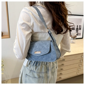 Close-up of blue denim textured shoulder bag with a gold metal buckle and stitching
