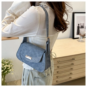 Detail shot of a blue denim texture shoulder bag with minimalist silver metal buckle