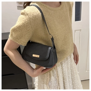 Detail view of a black minimalist underarm bag with gold metal buckle worn by a model