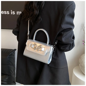 Detail of silver metallic handbag with bow buckle shown on shoulder of model