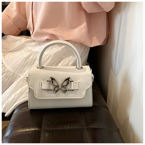 Close-up of a white leather handbag featuring a decorative gold bow buckle and top handle