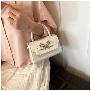 Close-up of white crossbody bag with silver butterfly buckle on pink shirt outfit