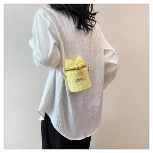 Detail of yellow quilted heart bucket bag with bow and gold chain on a model