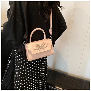 Pink faux leather crossbody bag with silver bow buckle worn on side, showing size and style