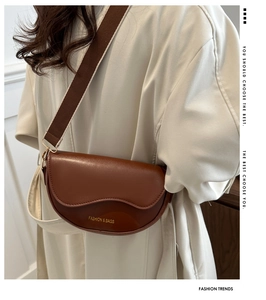 Détail d'un sac besace en cuir marron foncé avec large bandoulière sur un trench-coat blanc