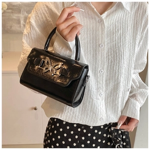 Close-up of a glossy black handbag featuring a silver butterfly metallic buckle detail