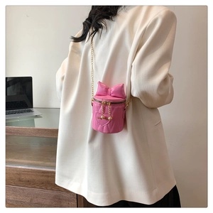 Close-up of pink quilted mini bucket bag with large bow and gold chain strap worn by a model