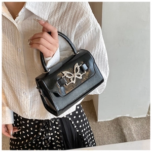 Detail of glossy black handbag featuring a silver butterfly buckle and high-shine finish