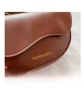 Détail du sac selle marron caramel avec rabat ondulé et lettrage doré décoratif