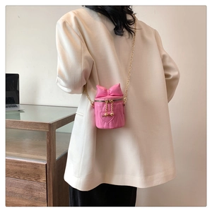 Pink cylinder bucket bag with bow detail and chain strap worn by a model