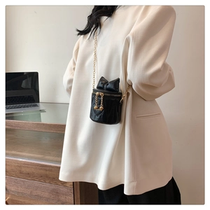 Detail of black leather heart-quilted crossbody bag with bow and gold chain on model