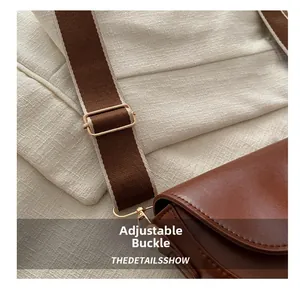 Détail de la boucle dorée réglable et de la large bandoulière en tissu sur le sac marron