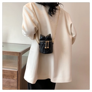 Detail of a black quilted cylindrical bucket bag with bow and gold chain on model