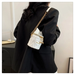 Close-up of white quilted mini bucket bag with gold chain strap on a black blazer