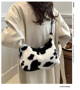 Detailed view of plush cow print shoulder bag with black leather strap on a beige coat