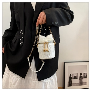 Close-up of white bucket bag with large bow, heart quilting and golden chain strap