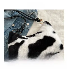 Detail shot of plush faux fur cow print shoulder bag with black knotted strap and gold hardware