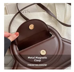 Macro detail of dark brown leather handbag showing gold magnetic buckle and stitching