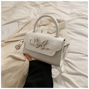 Detailed view of white leather crossbody bag with silver bow ornament and top handle