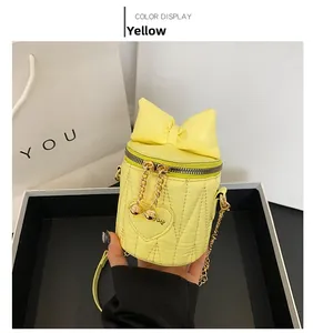 Close-up of yellow cylinder bag with bow, heart quilting, and gold chain details