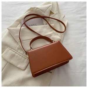 Detail of a brown vintage square handbag with a round handle and a slim crossbody strap