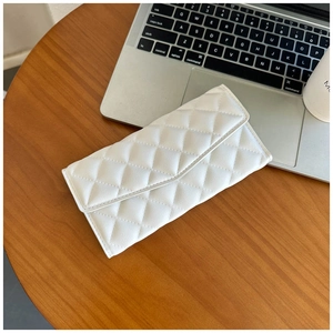 Detailed view of a white quilted leather handbag on a desk with a laptop and coffee cup