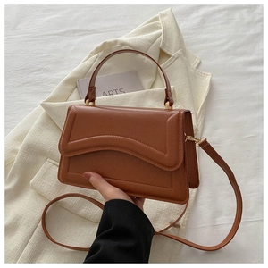 Detail of caramel brown faux leather handbag with wavy flap and thin shoulder strap