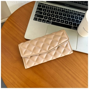 Detail of beige quilted wallet with diamond stitching on a wooden table setup