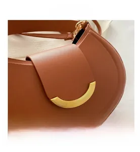 Detail view of a brown leather saddle bag with a unique gold semi-circular metal buckle