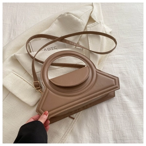 Detail of a brown trapezoid handbag with a unique hollow handle and smooth PU leather