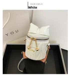Detail of white quilted bucket bag featuring a decorative bow and gold chain strap