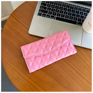 Pink quilted leather long wallet with diamond stitching on a desk workspace