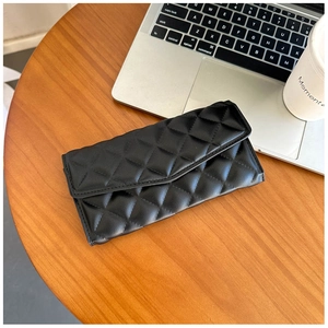 Flat lay of a black quilted leather clutch on a wooden desk with a laptop and coffee cup