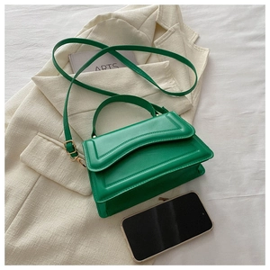 Detail of a bright green minimalist crossbody bag on a beige blazer with a slim strap