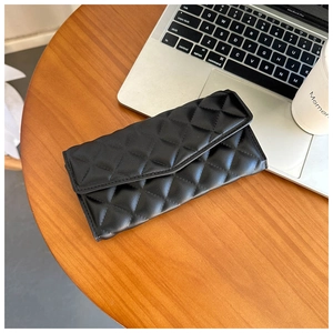 Close-up of black quilted diamond pattern wallet with flap design on a wooden desk