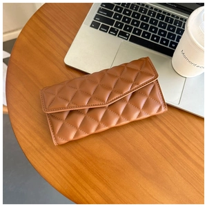 Brown quilted leather wallet on a wooden desk next to a coffee cup and laptop