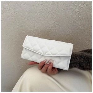 Detailed view of elegant white quilted clutch bag with diamond stitching held by hand