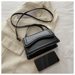 Top-down view of black shoulder bag with wavy flap detail on a white blazer