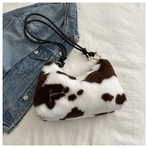 Detail of plush cow print underarm bag with black woven rope strap and gold metal accents