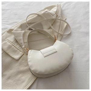Top view of white leather half-moon shoulder bag with gold hardware on a beige blazer