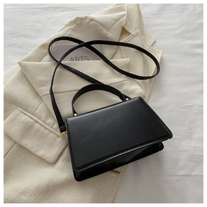 Detail view of black leather trapezoid bag with gold hardware and top handle on beige suit