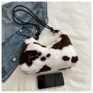 Detail of plush cow print underarm bag with knotted strap next to a phone for scale