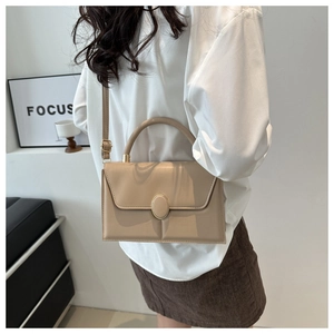 Détail d'un sac à main beige rectangulaire avec boucle dorée porté par un mannequin