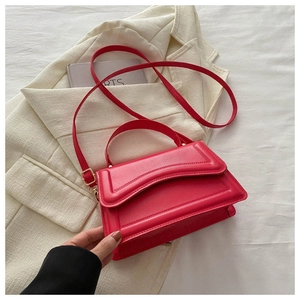 Detail view of the red leather crossbody bag with curved flap on white suit background